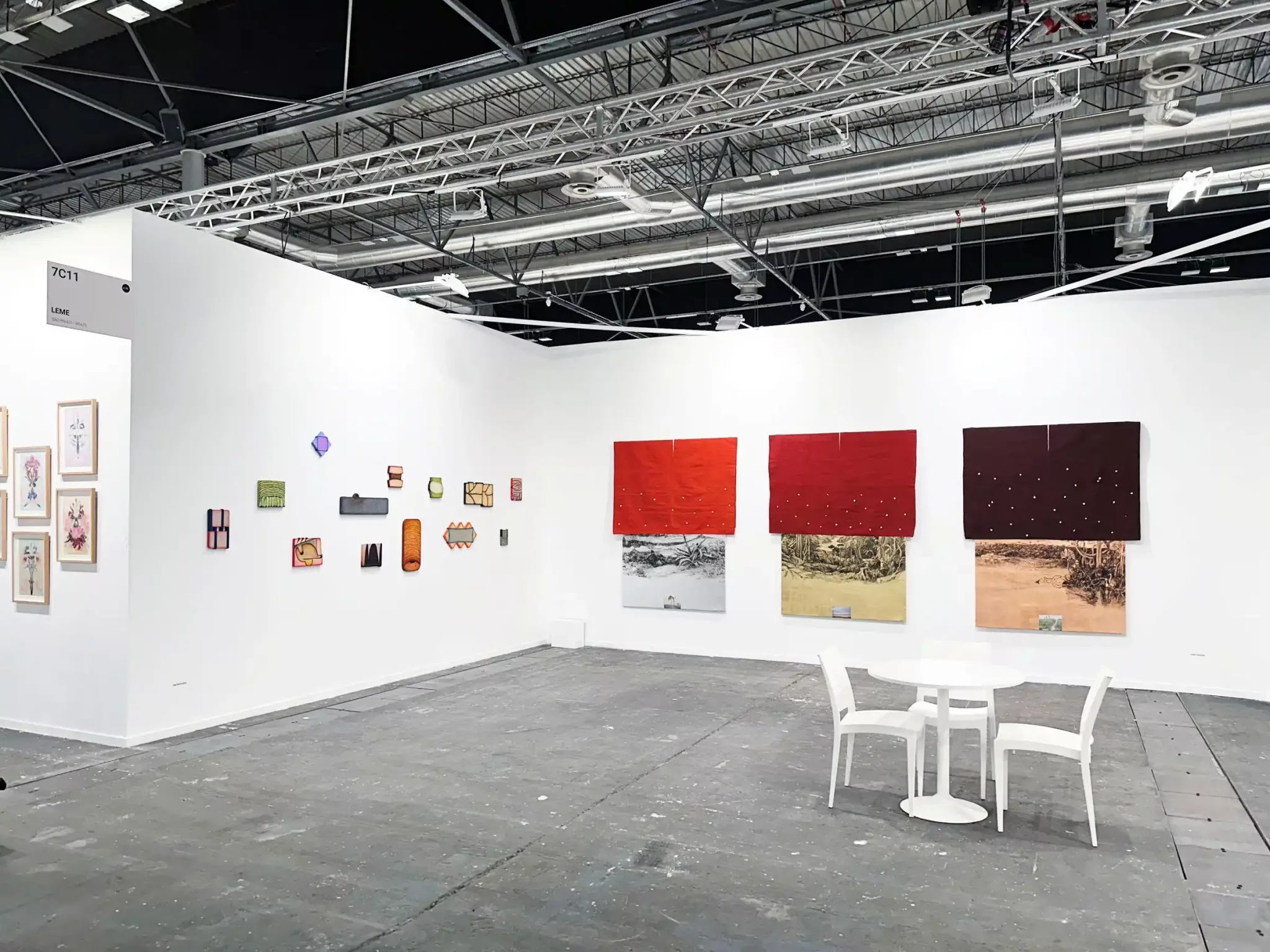 Estande da Galeria Leme na ARCOmadrid 2025 com obras contemporâneas em parede branca, mesa e cadeiras brancas, teto industrial exposto.