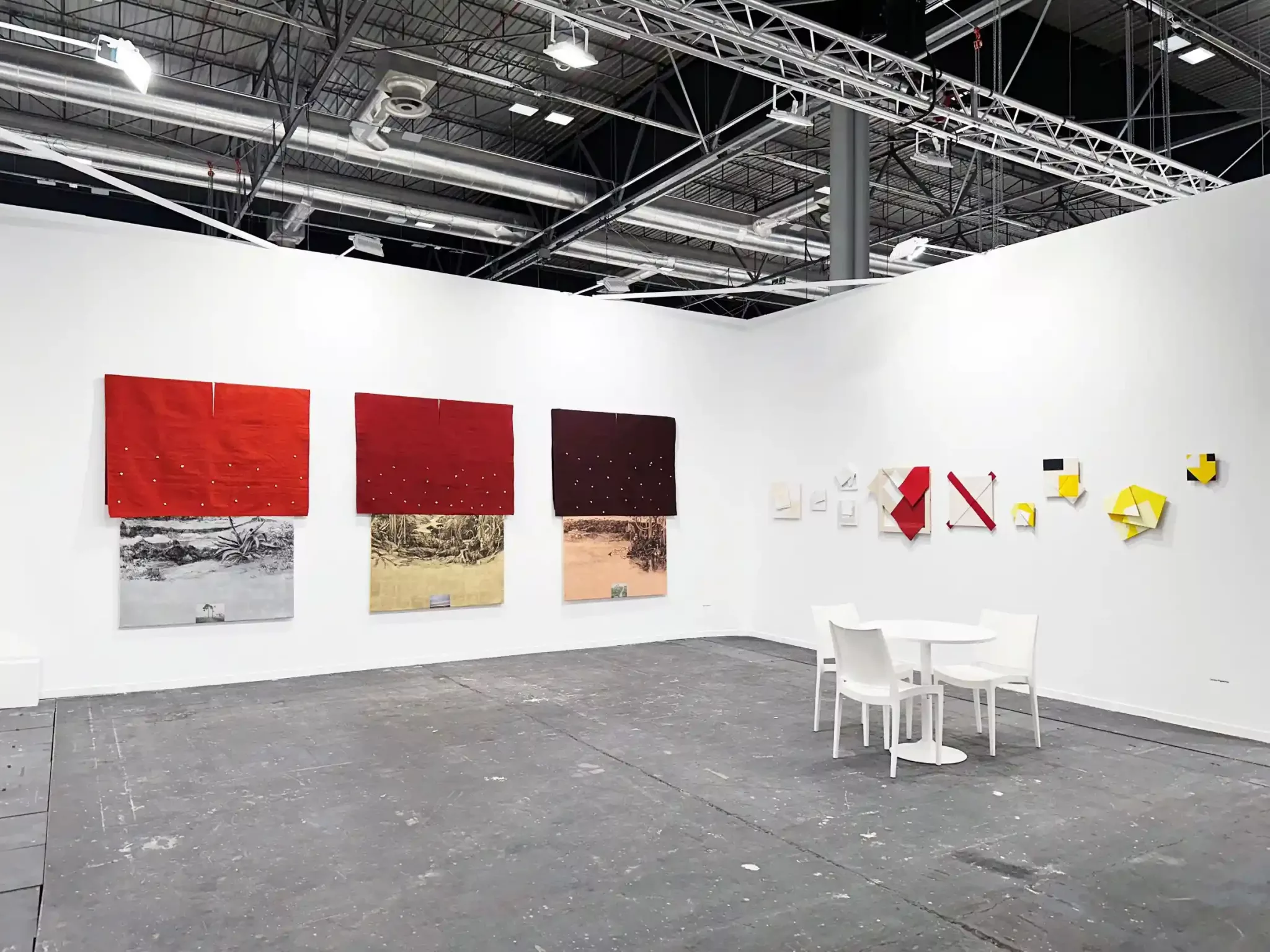 Estande da Galeria Leme na ARCOmadrid 2025 com obras abstratas em parede branca, mesa e cadeiras brancas, teto industrial exposto.